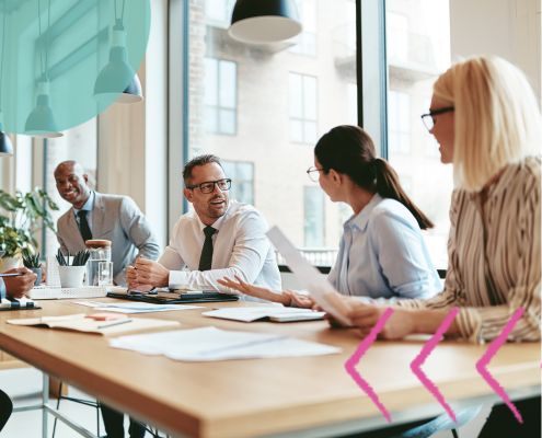 This is an image of five work colleagues sat at a table talking to eachother
